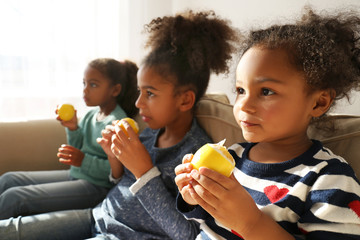 Three cute African girls sitting on sofa and eating lemons