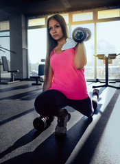 Young confident woman doing exercise with dumbbells in fitness gym. Slim girl training