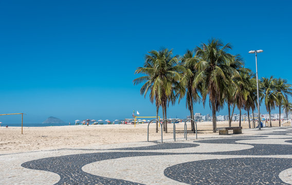 Copacabana beach with white sand, blue sky, green palms and mosaic floor, black and white Portuguese pavement in Rio de Janeiro, Brazil