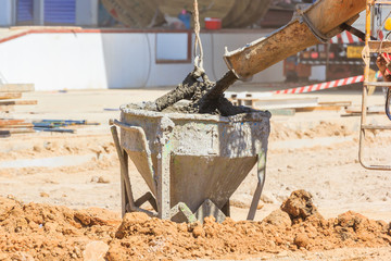 Concrete mixer truck pouring liquid concrete into the tower crane bucket at the construction site,...