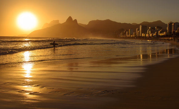 Golden sunset with Two Brothers Dois Irmaos Mountain and surfer silhouette at Ipanema Beach, Rio de Janeiro, Brazil
