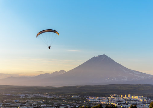 Paraglider flying over Petropavlovsk-Kamchatsky on the background of the cone of the volcano Koryaksky at sunset - Kamchatka, Russia