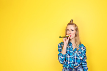 Young beautiful woman with party whistle on yellow background