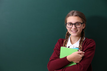 Teenage girl with books standing near green school blackboard