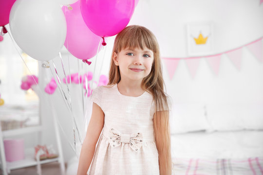 Cute girl with colorful balloons in room decorated for birthday party