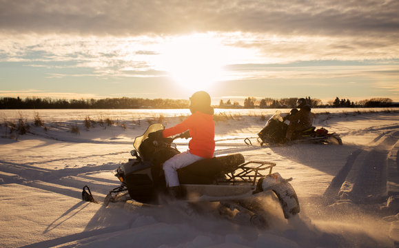 A father and his two gaughters riding two snowmobiles at sunset across a snow covered field in a winter landscape