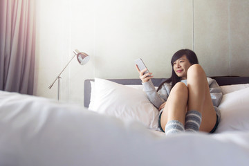 Asian woman Smile and Relaxing with Mobile Phone in Bed