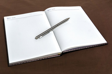 Notebook and silver pen on brown cloth background.