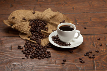 White cup of coffee with beans on wooden table