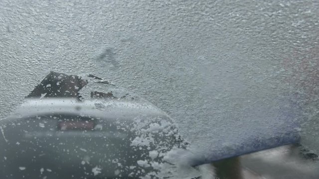 Someone scraping ice off the car's windscreen. He works hard to takes off the freezing rain too. This footage made from inside the car.
