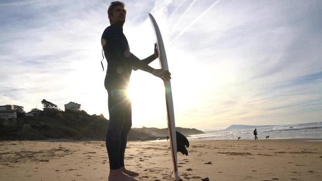 Surfer standing on sandy beach, sunset light
