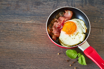 Fried egg and bacon in a frying pan, top view