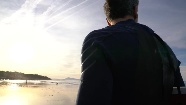 Surfer with surfoard walking on the beach at sunset