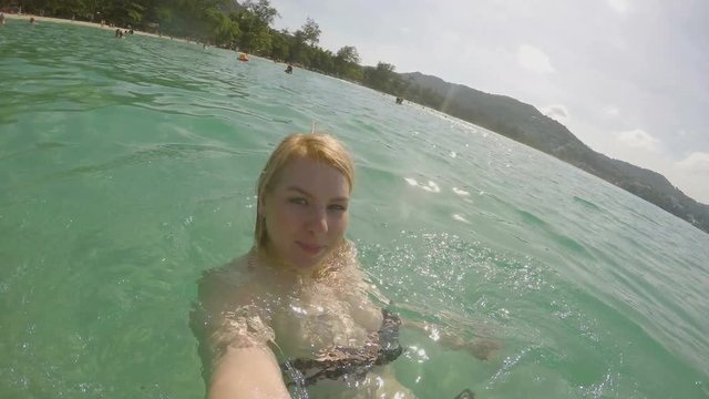Blonde woman taking selfie video on a beach