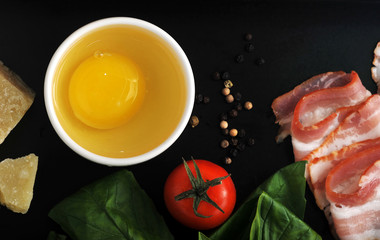 raw egg in a dish and the bacon, Basil leaves and tomato