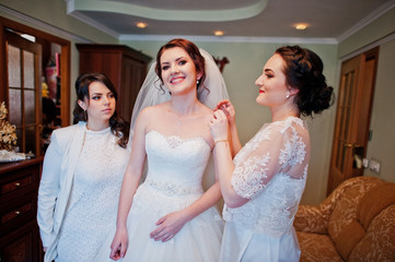 Bridesmaids helping dressed bride on wedding day at morning.