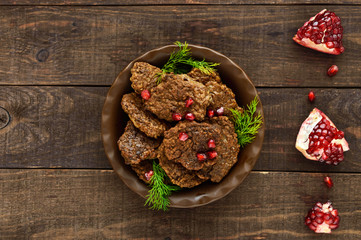 Juicy liver cutlets with pomegranate seeds on a ceramic plate on a dark wooden background. The top view