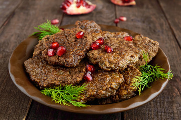 Juicy liver cutlets with pomegranate seeds on a ceramic plate on a dark wooden background.