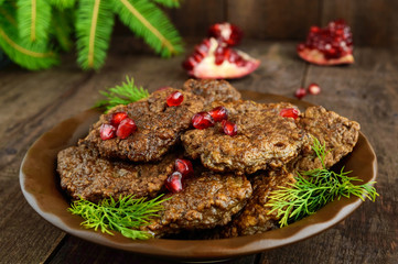 Juicy liver cutlets with pomegranate seeds on a ceramic plate on a dark wooden background.