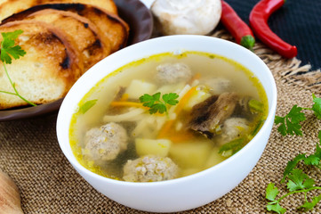 Light soup with dried mushrooms, meatballs and maccheroni in a white bowl. Close-up.