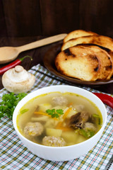 Light soup with dried mushrooms, meatballs and maccheroni in a white bowl. Vertical view.