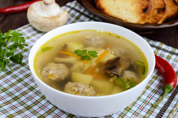Light soup with dried mushrooms, meatballs and maccheroni in a white bowl. Close-up.