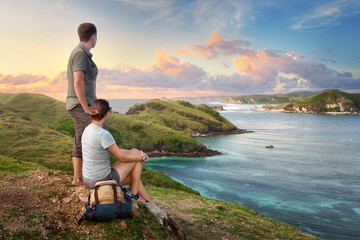 Naklejka na ściany i meble Couple hikers with backpacks enjoying sunset at mountain coast