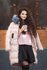 Curly hairstyle young woman alone standing near cafe and holding a cup of coffee