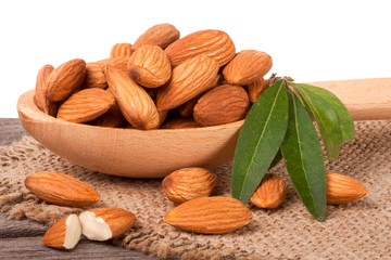 heap of peeled almonds with leaf in a wooden spoon on table isolated white background