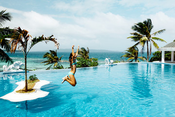 Child jumping in infinity pool with ocean view