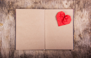 Open notebook with blank pages and Valentine origami. Red origami heart on a clean page. The concept of Valentine's Day. Copy space