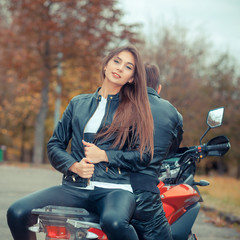 Fototapeta na wymiar Pretty girl with a biker posing near a sports bike. Beautiful couple with a motorcycle at sunset
