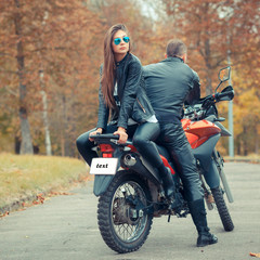 Fototapeta na wymiar Pretty girl with a biker posing near a sports bike. Beautiful couple with a motorcycle at sunset