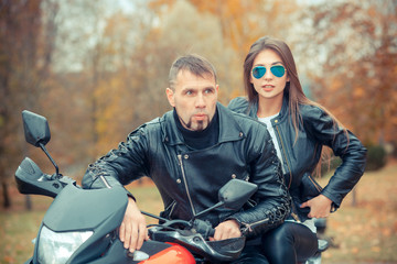 Fototapeta premium Pretty girl with a biker posing near a sports bike. Beautiful couple with a motorcycle at sunset