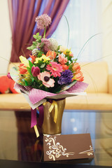 Brown festive card stands before golden vase with colorful bouqu