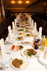 Rolls of white serviettes stand on dinner plates on long table
