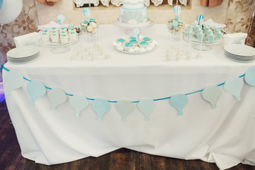 Garland of blue paper balloons hangs on white table with sweets