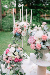 White candleholder stands among bouquets of peonies and roses on