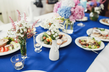 Little vases with white and pink field flowers stand on dinner t