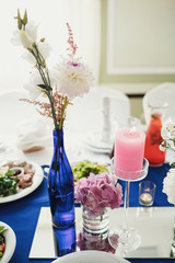 Obraz na płótnie Canvas Beautiful flowers in blue bottle of wine stands on glass tray