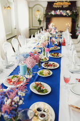 Plates with salads and vases with flowers stand on blue cloth