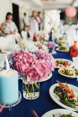 Pink hydrangeas stand in glass vase on blue dinner table