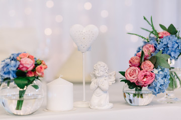 Figures of praying angel and ange stand between vases with roses