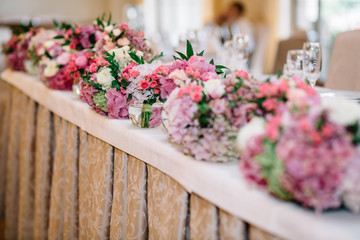 Pink and violet bouquets stand in the row on white dinner table