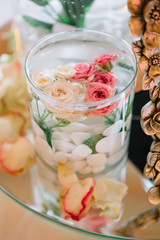 Glass vase with white stones and roses in water