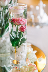 Glass vase with white stones and roses in water and little candl