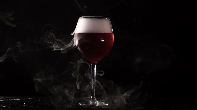 On a black background with glasses of red liquid coming out steam. In a glass jar on a high pedicle with a burgundy wine is a decorative pair that with a sudden breath begins to disappear and dissolve