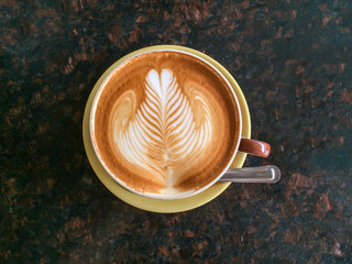 Latte art in cup of hot latte coffee with black marble table background