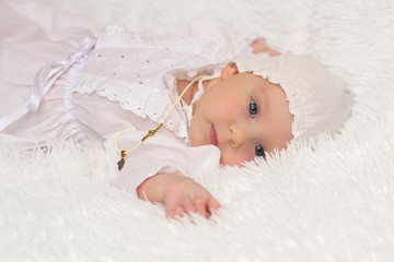 little girl in a white dress and hat, after baptism, laying on his back on a white blanket on a...