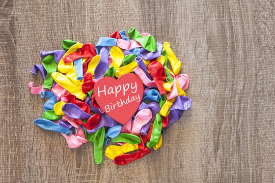 Happy Birthday card with a red heart on colorful deflated balloons. Table top view
